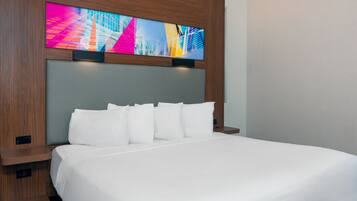 A hotel room with a large bed, white bedding, a wooden headboard, and a colorful artwork above the bed.