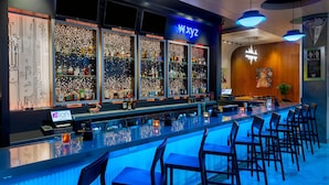 A bar area with a long counter, multiple shelves of bottles, and several chairs.