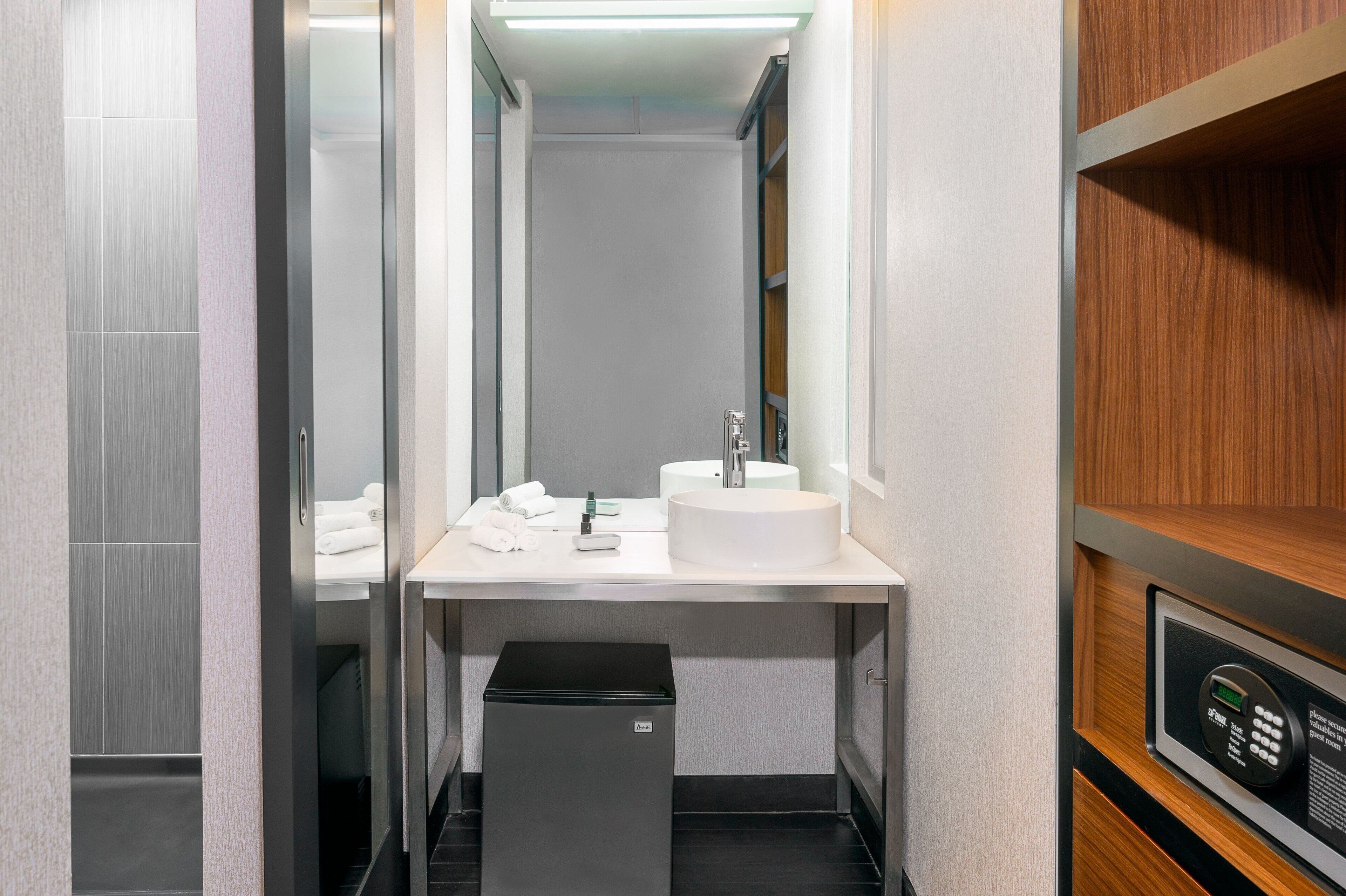 Een moderne badkamer met een witte wastafel, spiegel en een klein prullenbakje.