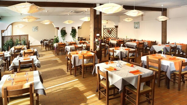 A spacious restaurant with multiple dining tables, wooden chairs, and hanging pendant lights. - Motel Monterosa (Vogogna)