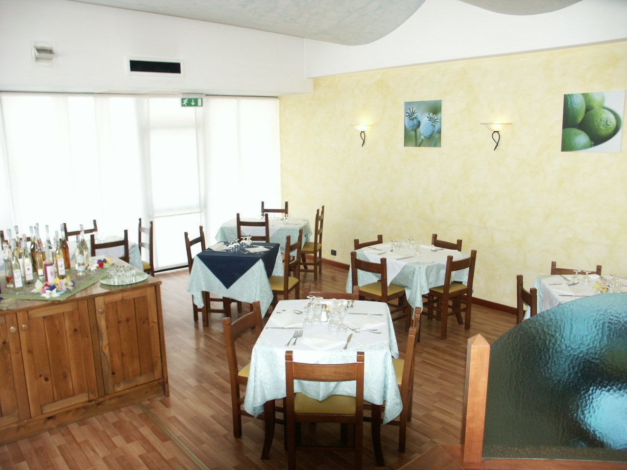 Un ristorante con tavoli e sedie in legno, una zona bar con bottiglie e una parete decorata con quadri.