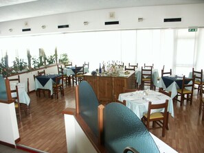 Un restaurant doté de nombreuses tables et chaises, d’un bar central et de grandes fenêtres laissant entrer la lumière naturelle.
