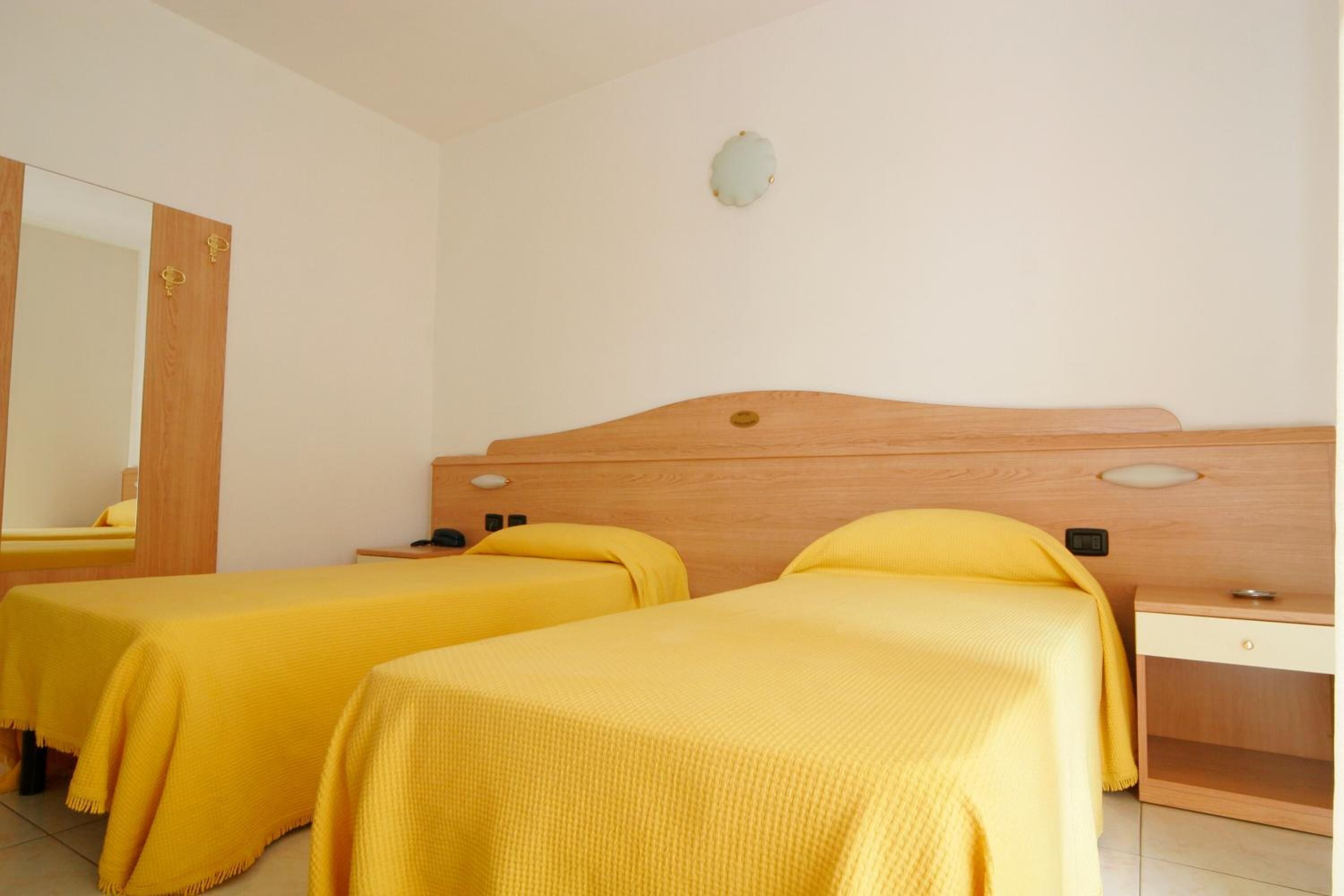 Camera d'albergo con due letti singoli, una testiera in legno, un comodino e uno specchio.