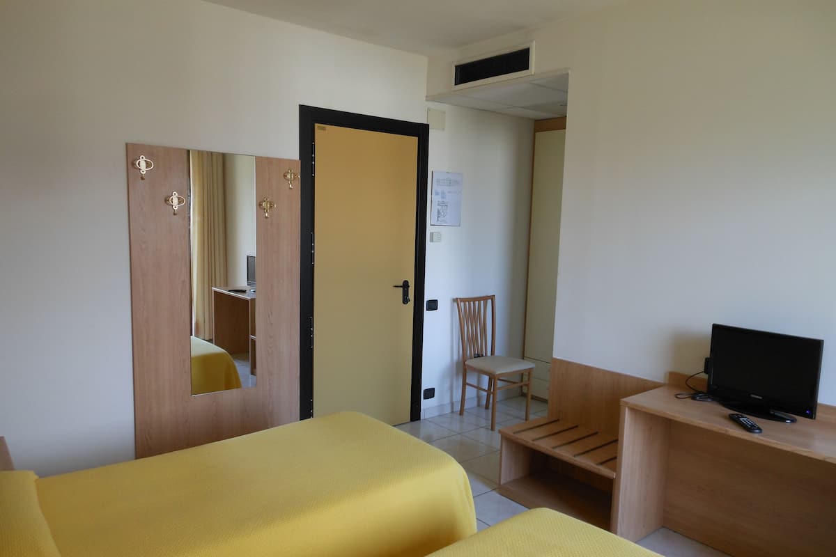 A hotel room with two beds, a desk with a TV, a chair, and a wooden wardrobe.