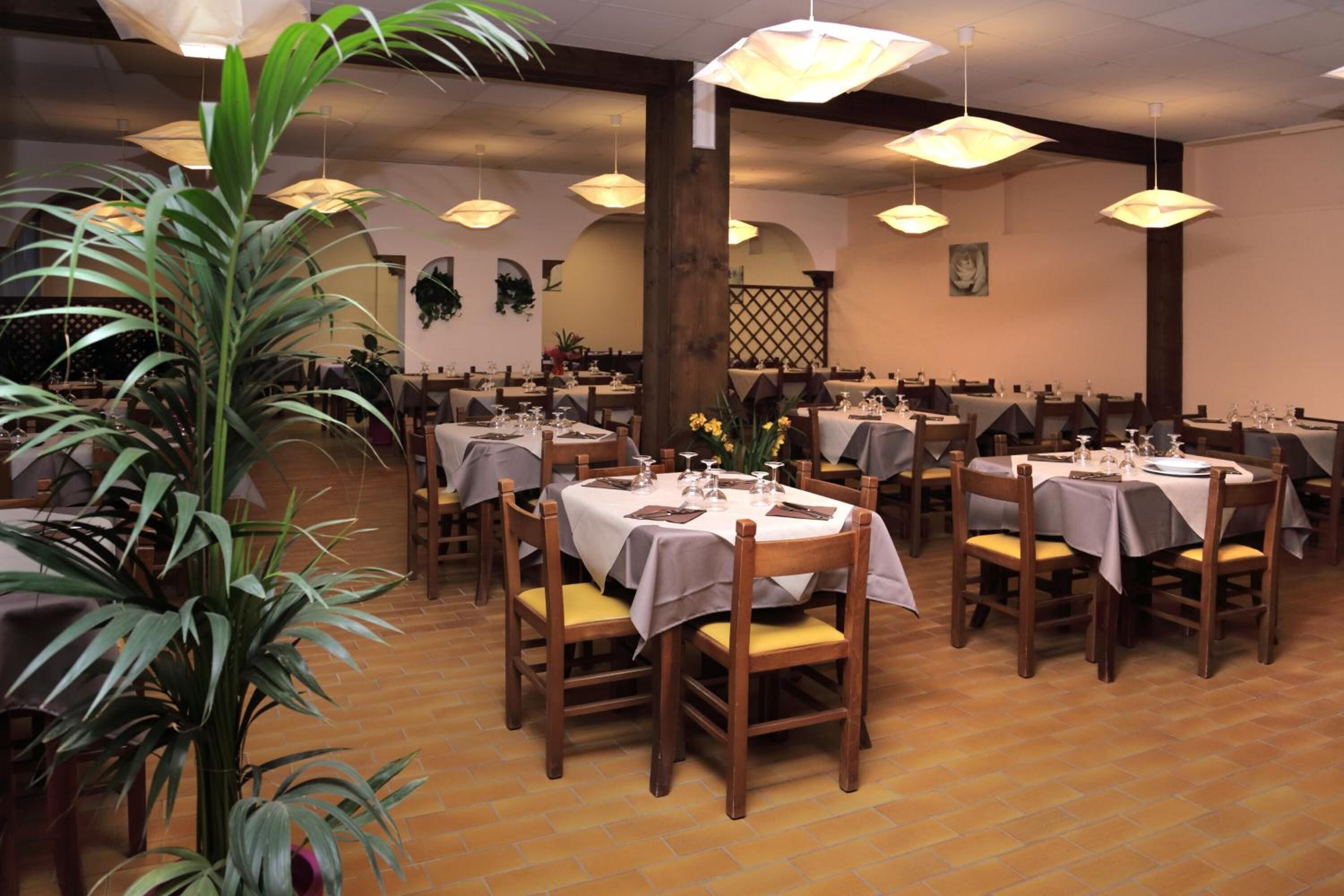 A restaurant with round tables, wooden chairs, and hanging pendant lights.