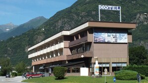 A motel with a signboard, a large advertisement, and a mountainous backdrop. - Motel Monterosa (Vogogna)