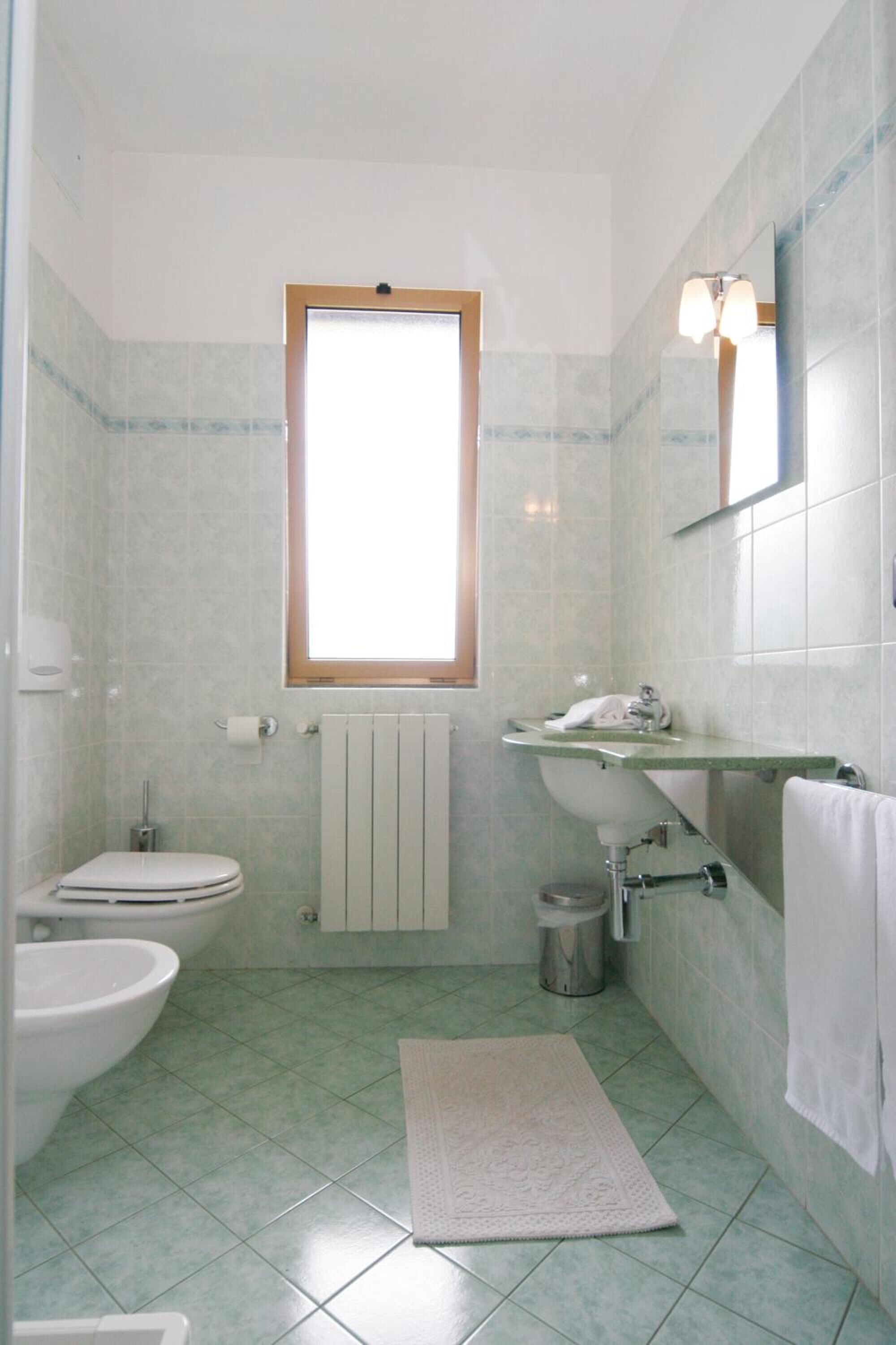 A bathroom with a toilet, bidet, sink, and a window.