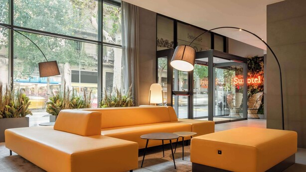 A modern hotel lobby with a large sofa, a round table, and a lamp. - Petit Palace Trencadis (Barcelona)