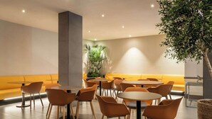 A modern dining area with round tables and orange chairs, a yellow cushioned bench, and a large potted plant. - Petit Palace Trencadis (Barcelona)