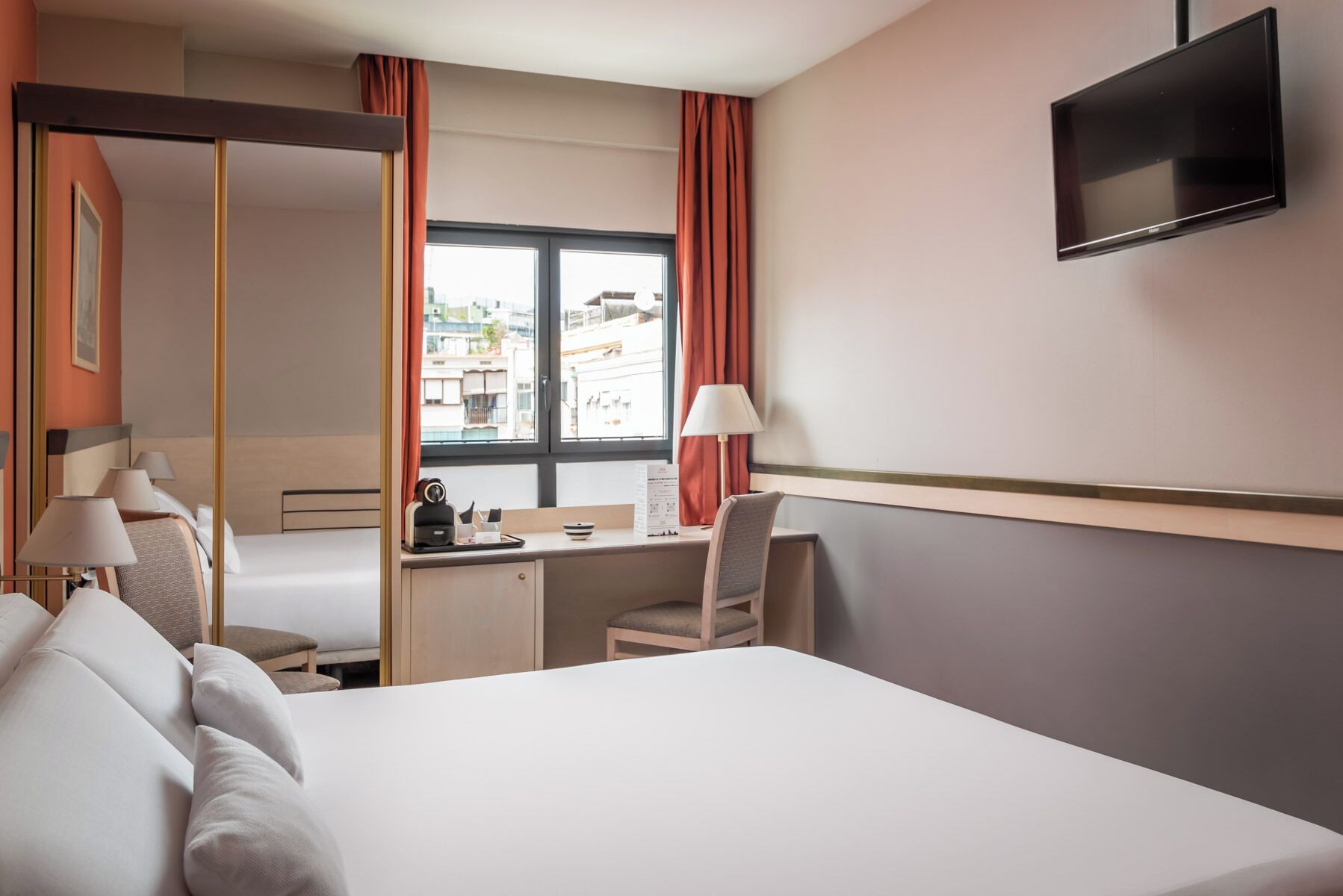 Una habitación de hotel con cama, escritorio, silla, televisor y ventana con cortinas.