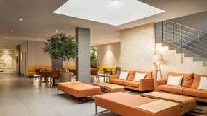 A modern lobby with orange sofas, a large plant, and a staircase. - Petit Palace Trencadis (Barcelona)