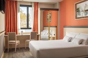 Una habitación de hotel con cama, dos sillas, un escritorio y una ventana con cortinas.