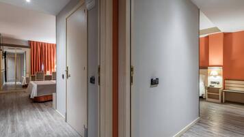 A hotel room with a bed, a desk, and a chair. There is a door with a handle and a light switch on the wall.