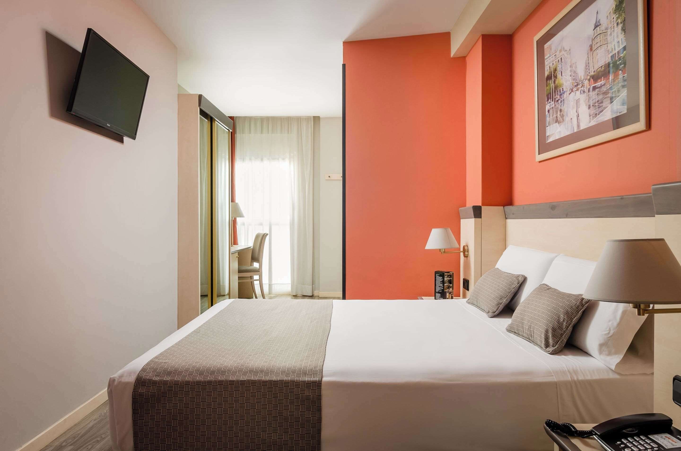A hotel room with a bed, bedside lamps, a telephone, and a television on the wall.