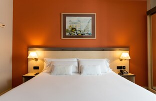 A hotel room with a large bed, two bedside lamps, a painting on the wall, and a telephone on the nightstand.