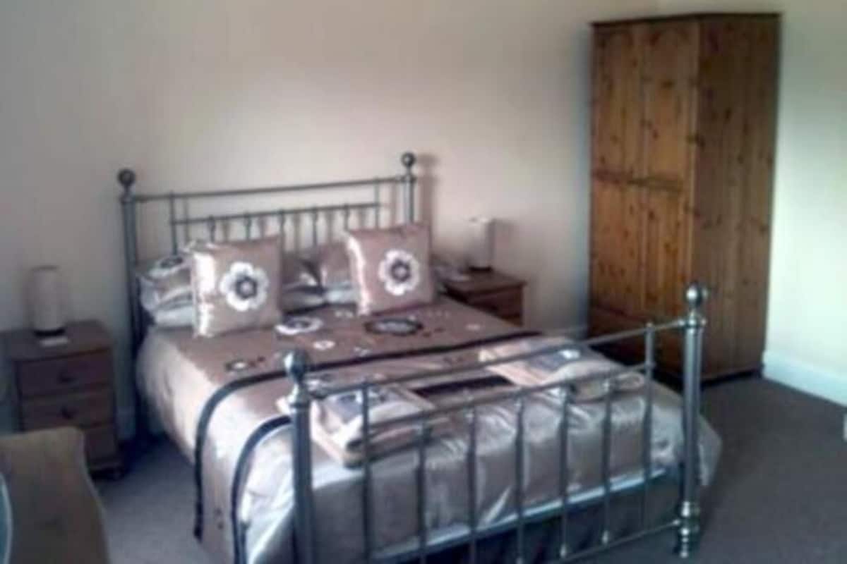 A bedroom with a metal bed frame, a wooden wardrobe, and a bedside table with a lamp.