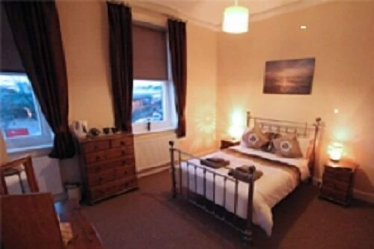 A bedroom with a bed, dresser, nightstands, and a window with curtains.