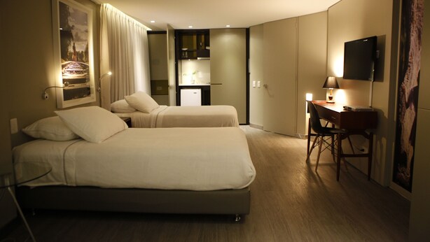 Habitación de hotel con dos camas, un escritorio, una silla, un televisor y una pequeña cocina.