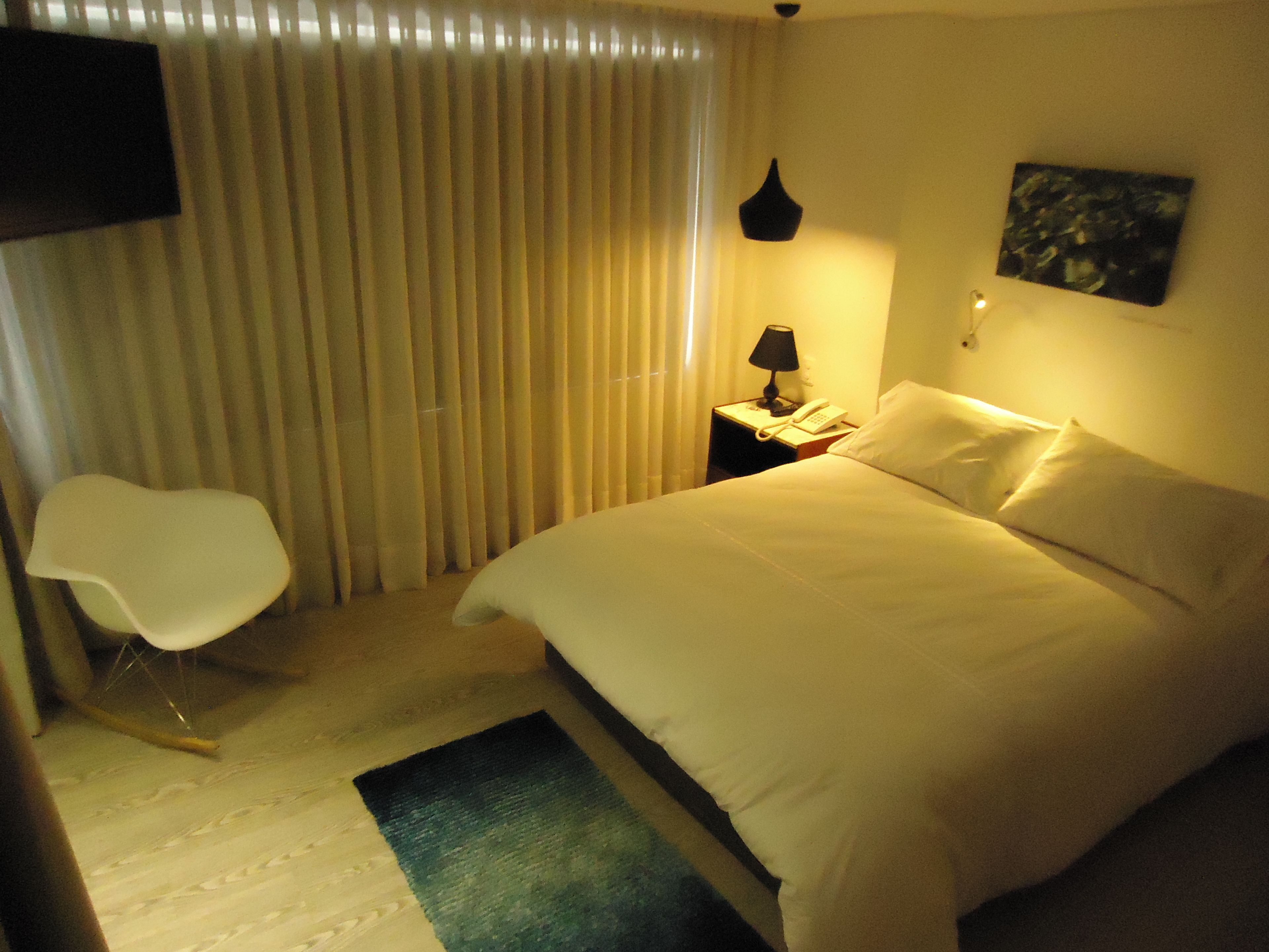 Une chambre d’hôtel avec un lit, une chaise, une table de chevet avec une lampe, un téléphone et un tableau au mur.