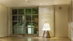 Un interior moderno con un cristalero que da a un jardín, una silla blanca y un panel informativo fijado a la pared.