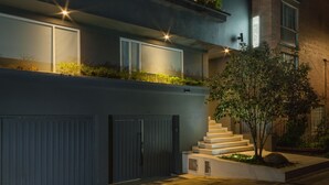 Un edificio moderno con fachada oscura, una escalera visible y un pequeño árbol en primer plano.