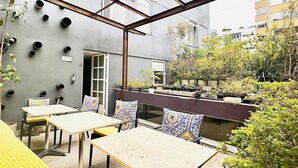Una terraza en la azotea con mesas y sillas, techo de cristal y plantas en macetas.