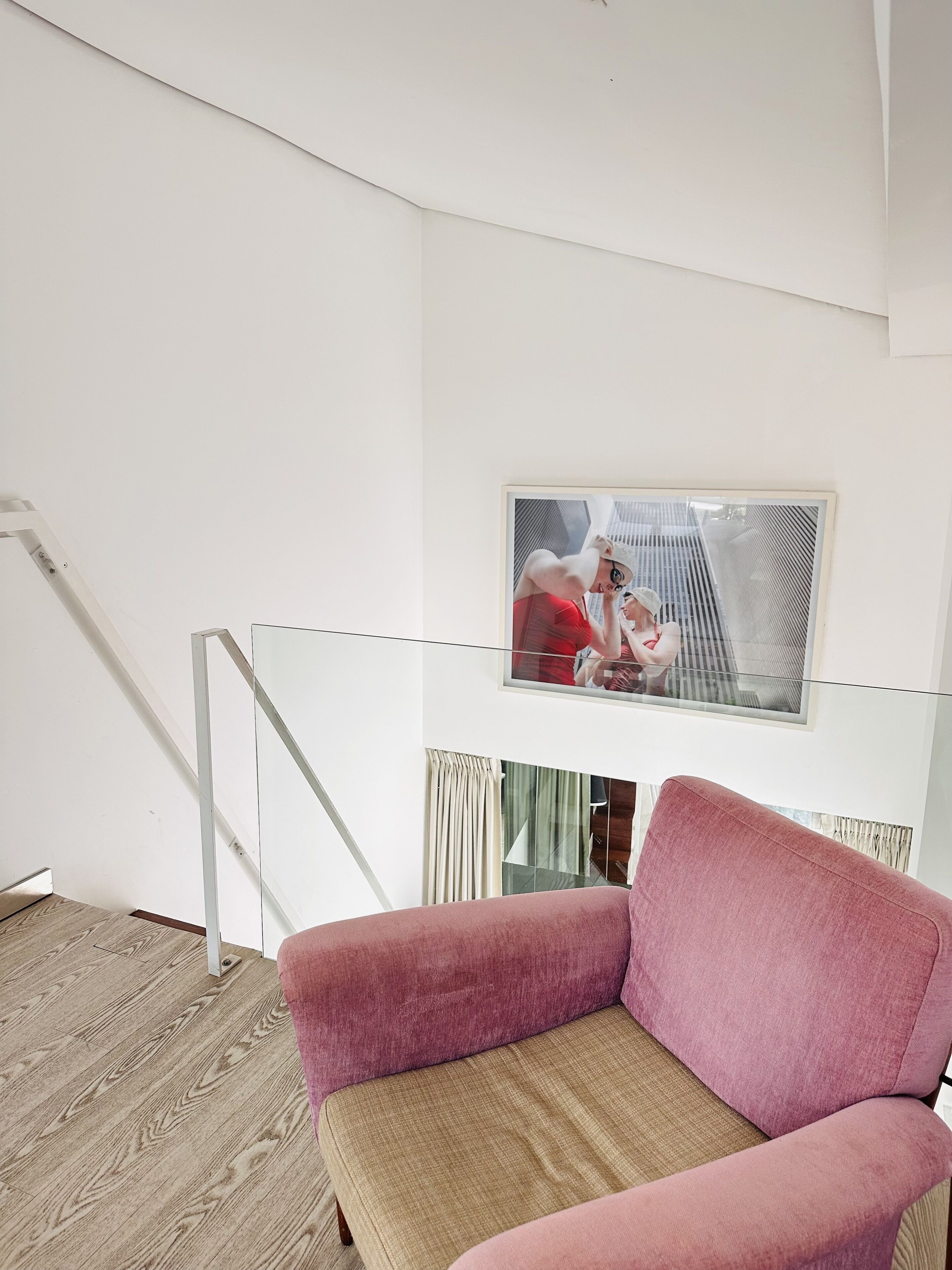 Una sala de estar moderna con un sofá rosa, piso de madera, una mesa de vidrio y un cuadro en la pared.