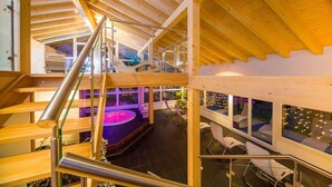 A multi-level wooden interior with a glass staircase, a hot tub, and seating areas. - Christiania Wellness Hotel (Saas Almagell)