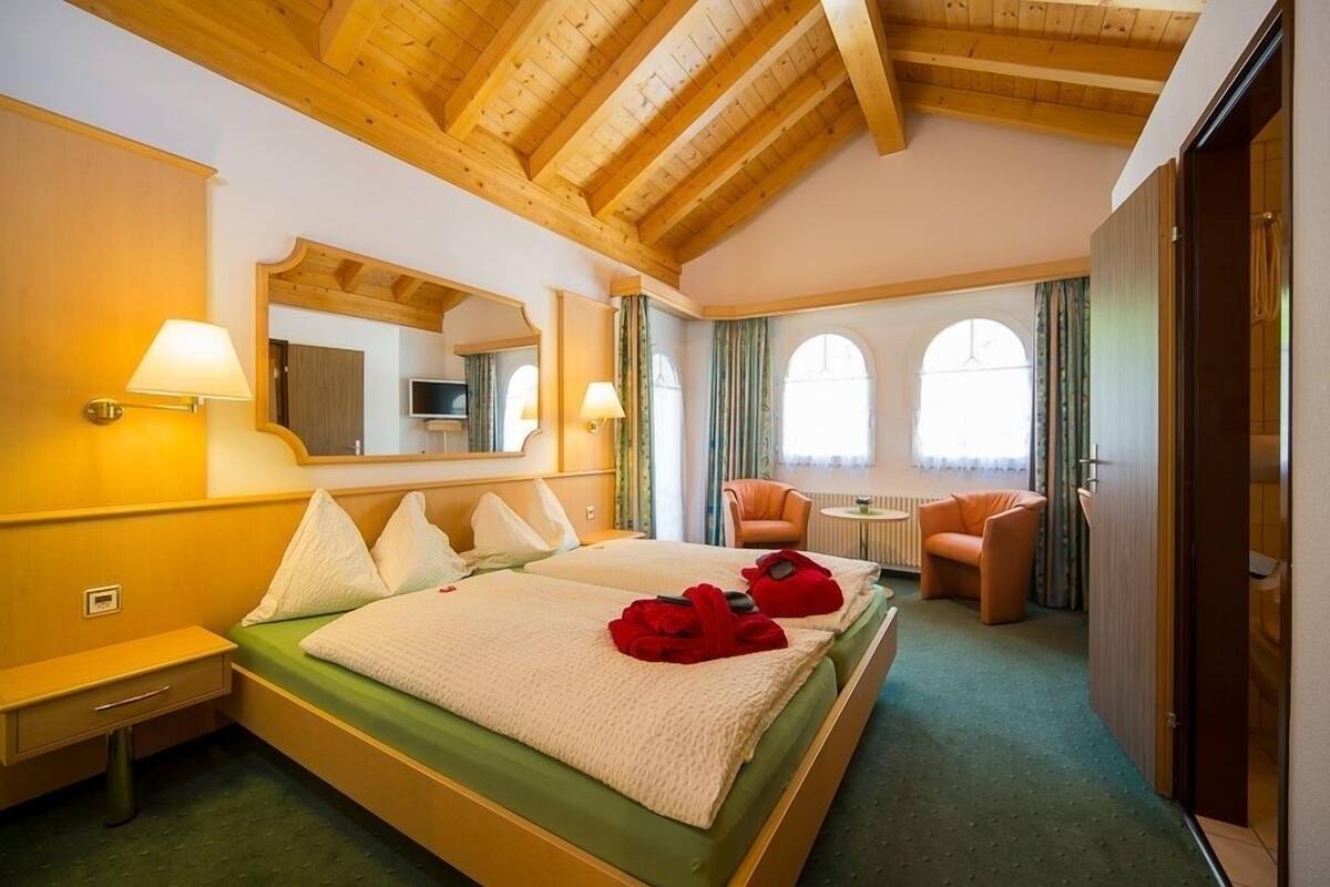 A hotel room with a large bed, two chairs, a small table, and a mirror.