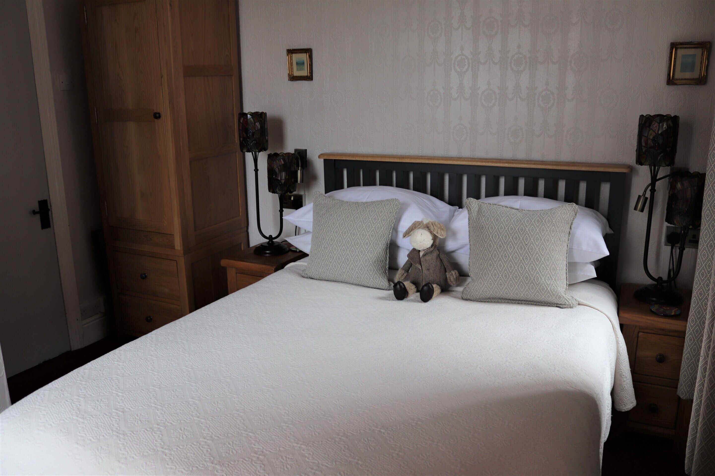 A neatly made bed with a plush toy, a wooden headboard, and two bedside lamps.