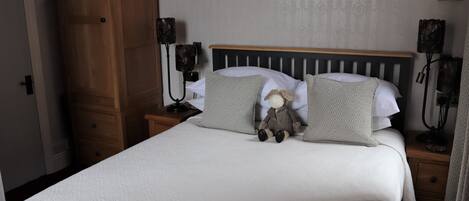 A neatly made bed with a plush toy, a wooden headboard, and two bedside lamps.
