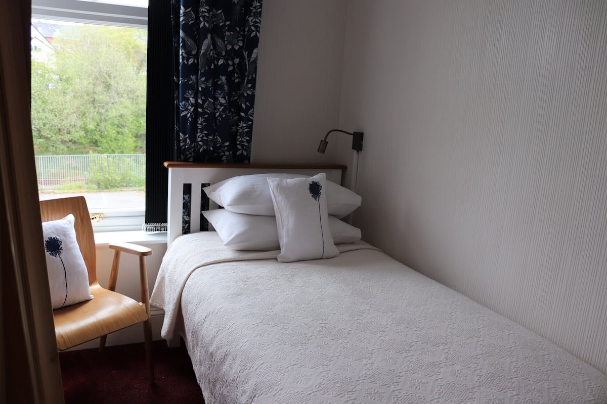 Ein Schlafzimmer mit Bett, Stuhl, Fenster mit Vorhängen und Nachttisch.