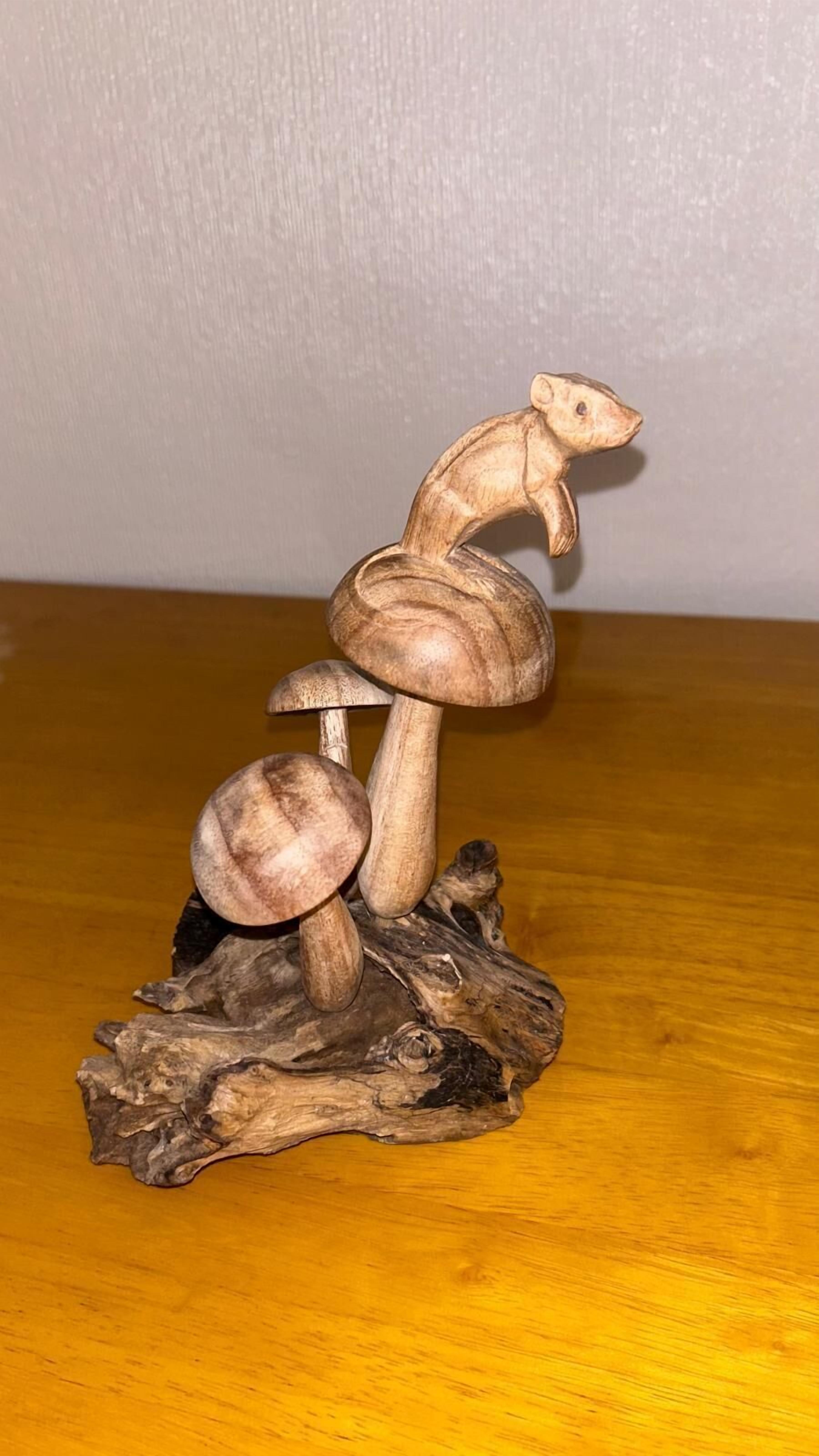Una escultura de madera de un oso sobre un hongo, colocada sobre un trozo de madera a la deriva.