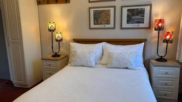 A neatly made bed with white linens and two nightstands, each with a stained glass lamp. There are framed pictures on the wall above the bed.