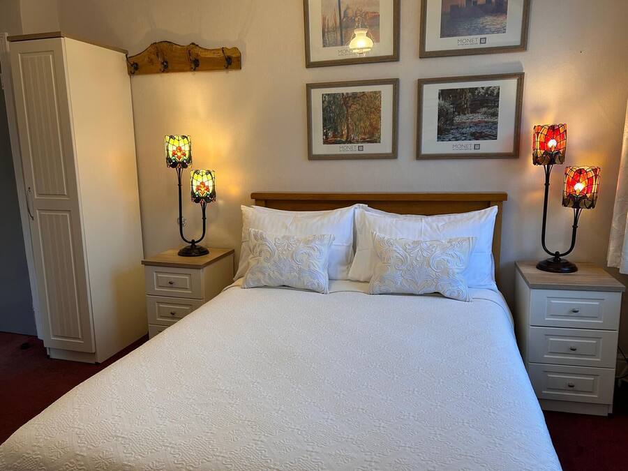 A neatly made bed with white linens and two nightstands, each with a stained glass lamp. There are framed pictures on the wall above the bed.