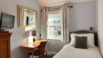 Un dormitorio con cama, escritorio, silla, televisor, ventana con cortinas y vistas al exterior.