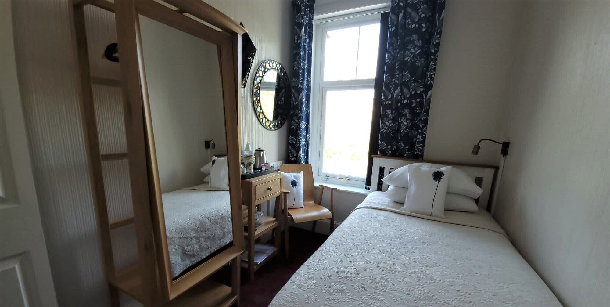 Un dormitorio con dos camas, un armario de madera, una mesita y una ventana con cortinas.