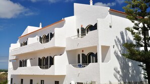 A white building with multiple balconies and arched windows, set against a clear blue sky. - Tonel Apartments (Vila do Bispo)