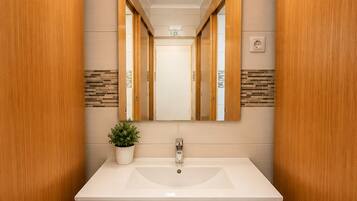 A bathroom with a white sink, wooden cabinets, a mirror, and a potted plant.