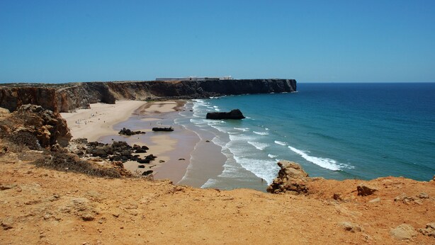 A coastal landscape with a sandy beach, rocky cliffs, and a clear blue sky. - Tonel Apartments (Vila do Bispo)