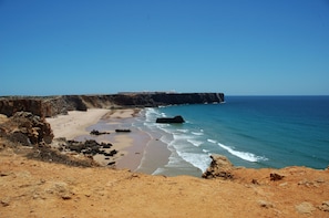A coastal landscape with a sandy beach, rocky cliffs, and a clear blue sky. - Tonel Apartments (Vila do Bispo)