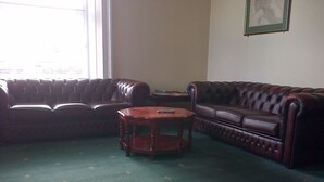 A living room with a green carpet, two leather sofas, and a wooden coffee table. - Aurora Hotel & Italian Restaurant (Nairn)