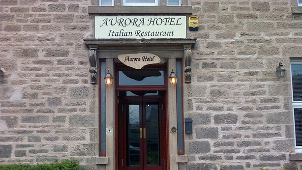 The exterior of Aurora Hotel, an Italian Restaurant with a stone facade, wooden entrance, and a sign above the door. - Aurora Hotel & Italian Restaurant (Nairn)
