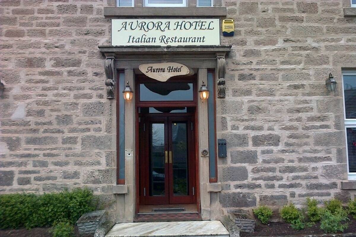 The exterior of Aurora Hotel, an Italian Restaurant with a stone facade, wooden entrance, and a sign above the door.