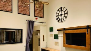 A bedroom with a bed, a wooden desk, a clock, and a window with curtains. - The Bull Inn Pub (Reading)