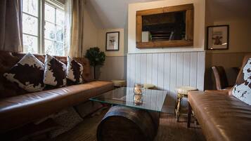 Een gezellige woonkamer met een bruine leren bank, een glazen salontafel en een houten vat.
