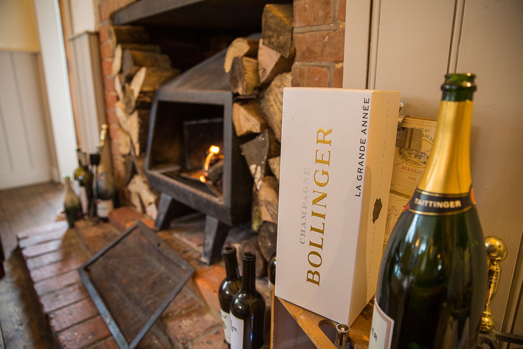 Eine Flasche Bollinger Champagner, eine Schachtel mit dem Aufdruck 'Bollinger La Grande Année' und ein Kamin mit Holzscheiten.