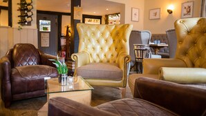 A cozy living room with leather sofas, a tufted armchair, and a glass coffee table. - The Bull Inn Pub (Reading)