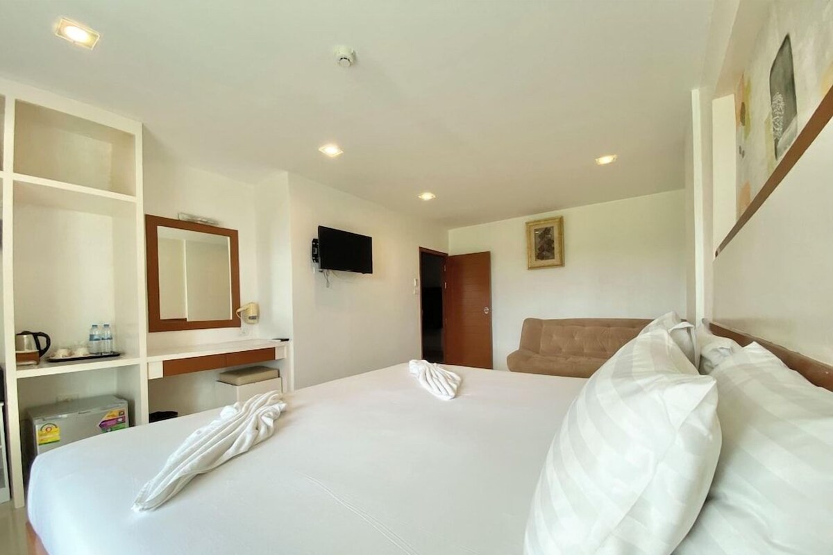 Une chambre d’hôtel avec un grand lit, un téléviseur fixé au mur, une tête de lit en bois et une armoire avec un miroir.