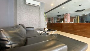 A modern lobby with a leather sofa, a glass table, and a reception desk with a brick accent wall. - Patong Platinums (Patong)